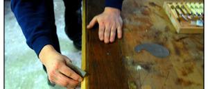 Ein Tischler bearbeitet ein altes Möbelstück und verhilft ihm zu neuem Glanz.