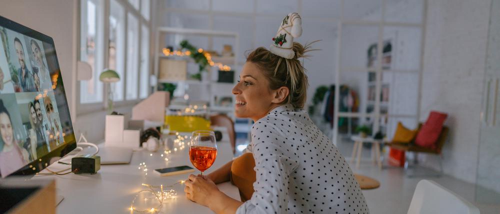 Photo of a young woman celebrating Christmas by having a virtual Christmas party with her friends; drinking wine, celebrating Christmas and holidays apart from friends and family, and practicing social distancing.