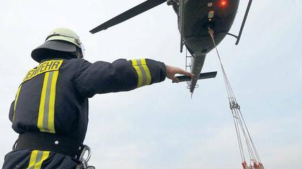 Ein Feuerwehrmann weist einen Hubschrauber ein, der Sandsäcke zur Abdichtung eines Deiches der Schwarzen Elster bei Mönchenhöfe transportiert.
