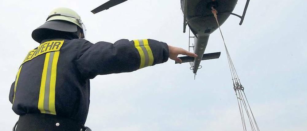 Ein Feuerwehrmann weist einen Hubschrauber ein, der Sandsäcke zur Abdichtung eines Deiches der Schwarzen Elster bei Mönchenhöfe transportiert.