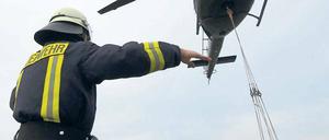 Ein Feuerwehrmann weist einen Hubschrauber ein, der Sandsäcke zur Abdichtung eines Deiches der Schwarzen Elster bei Mönchenhöfe transportiert.