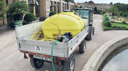 Ein Gärtner befüllt vor der Orangerie einen 1000 Liter Wassertank.