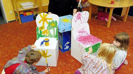 Papierveredlung. Klaus-Josef Oberbörsch sitzt im Kindergarten Frechdachse in Seelow an einem Papptisch, während Robin, Lena und Josefine (v.l.) falltbare Kindermöbel bemalen.