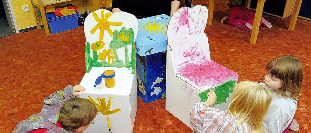 Papierveredlung. Klaus-Josef Oberbörsch sitzt im Kindergarten Frechdachse in Seelow an einem Papptisch, während Robin, Lena und Josefine (v.l.) falltbare Kindermöbel bemalen.