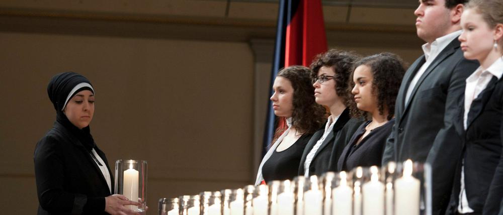 Eine junge Frau trägt am Donnerstag (23.02.12) im Konzerthaus in Berlin bei der zentralen Gedenkveranstaltung fuer die Opfer der Mordserie der terroristischen Vereinigung "Nationalsozialistischer Untergrund" (NSU) eine Kerze.