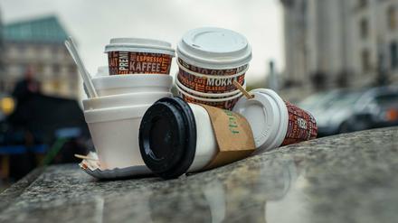 Einweg-Kaffeebecher und Plastikschalen stapeln sich an einem Gehweg.