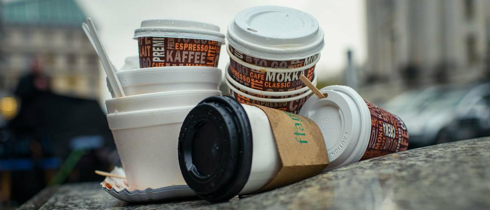 Einweg-Kaffeebecher und Plastikschalen stapeln sich an einem Gehweg.