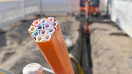 Farbige Leerrohre, in die später die Glasfaserkabel verlegt werden, ragen aus einem Graben auf einer Baustelle.