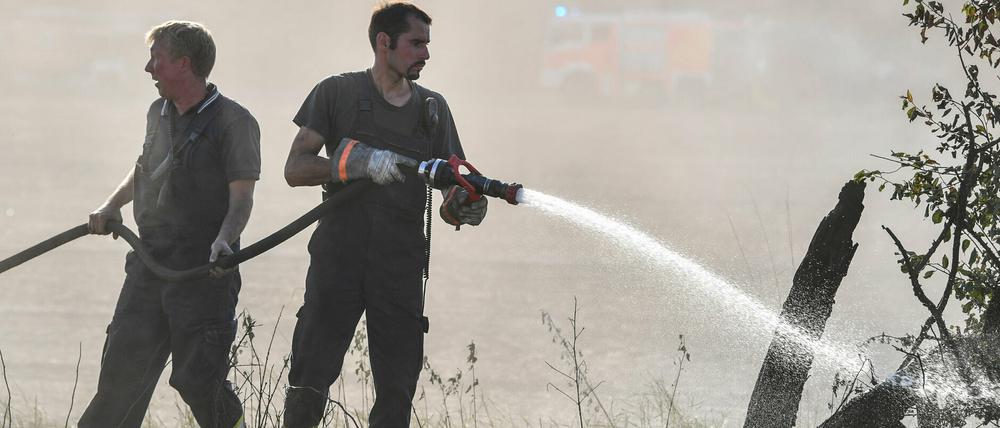 Feuerwehrmänner löschen Glutnester an einem Feldrand bei Storkow.