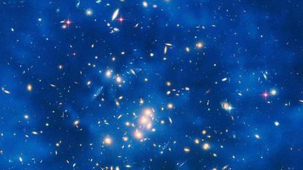 Was die Welt zusammenhält. Der Nachweis von schweren Gravitinos wäre ein wichtiger Schritt zur allenthalben gesuchten vereinheitlichten Theorie der Physik. Die Dunkle Materie, die aus diesen Teilchen bestehen könnte, macht sich nur über Gravitationseffekte bemerkbar. Die Aufnahme zeigt einen Ring Dunkler Materie in einem fünf Milliarden Lichtjahre entfernten Galaxienhaufen im Sternbild Fische. 