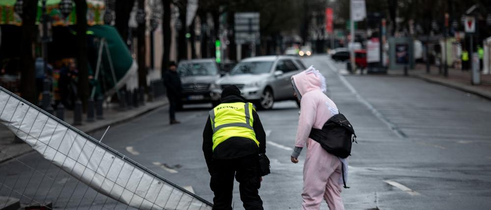 Ein Ordner und ein verkleideter Narr stehen an einem Bauzaun in Düsseldorf, der durch den Sturm umgeweht worden ist.