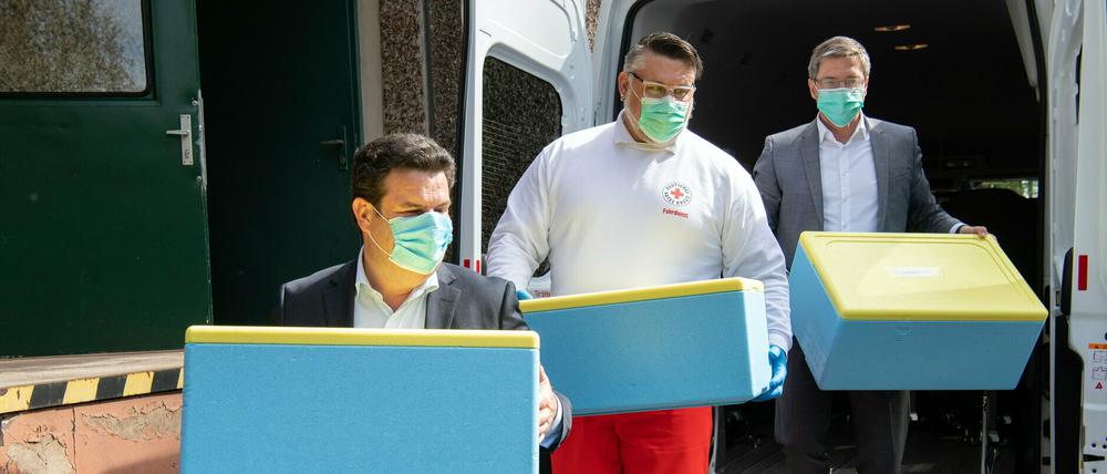 Bundesarbeitsminister Hubertus Heil (l.), DRK-Mitarbeiter Rico Wiemann und Potsdams Oberbürgermeister Mike Schubert tragen Thermoboxen für die Essensauslieferung in die Küche Bisamkiez. 