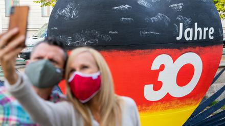 Ein Mann und eine Frau machen vor einem schwarz-rot-goldenen Herz mit der Aufschrift "30 Jahre" ein Selfie mit Maske.