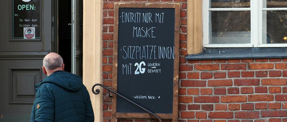 Ein Schild mit der Aufschrift "Eintritt nur mit Maske Sitzplätze innen mit 2G Genesen oder Geimpft" ist in der Potsdamer Innenstadt neben dem Eingang zu einem Café angebracht.
