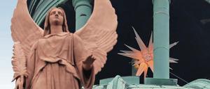 Seid behütet. Ein Weihnachtsstern leuchtet in der Kuppel der Nikolaikirche, davor einer der vier Turmengel, der seine Hand segnend über die Stadt hält.