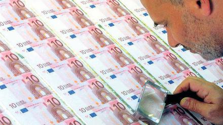 Ein Mann beugt sich mit einer Lupe in der Hand über einen Bogen mit Zehn-Euro-Geldscheinen.