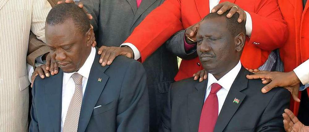 Kenyatta und Ruto knieen vor mehreren Priestern, die sie festhalten