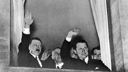 Der neu ernannte Reichskanzler Adolf Hitler grüßt nach der Machtübernahme am 30. Januar 1933 aus einem Fenster in Berlin heraus den vorbeiziehenden Fackelzug. Neben ihm stehen Innenminister Wilhelm Frick, Reichsminister Hermann Göring und der spätere Stellvertreter Hitlers, Rudolf Heß.