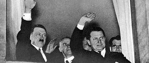 Der neu ernannte Reichskanzler Adolf Hitler grüßt nach der Machtübernahme am 30. Januar 1933 aus einem Fenster in Berlin heraus den vorbeiziehenden Fackelzug. Neben ihm stehen Innenminister Wilhelm Frick, Reichsminister Hermann Göring und der spätere Stellvertreter Hitlers, Rudolf Heß.