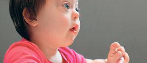 Ein Kind mit Downsyndrom sitzt am Tisch und malt ein Bild.