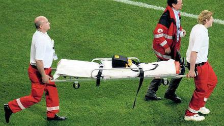 Drei Sanitäter tragen eine Trage über einen Fußballplatz