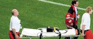 Drei Sanitäter tragen eine Trage über einen Fußballplatz