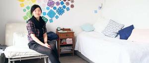 Eine Studentin sitzt in ihrem Wohnheim auf dem Sessel vor einer bunt dekorierten Wand.