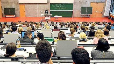 Studierende sitzen im Hörsaal und blicken nach vorne zum Rednerpult des Professors.