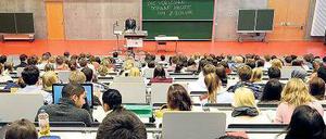 Studierende sitzen im Hörsaal und blicken nach vorne zum Rednerpult des Professors.