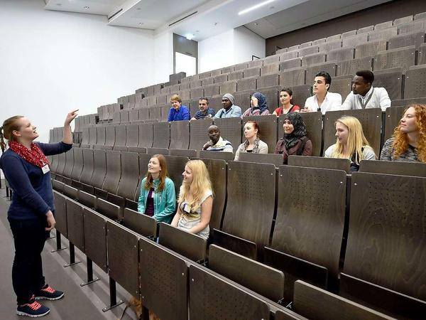 Eine Studentin steht in einem Hörsaal gestikulierend vor jungen Leuten.