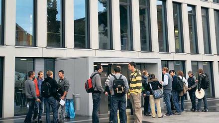 Studierende stehen vor einer Hochschule und unterhalten sich in kleinen Grüppchen.