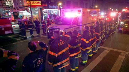 New Yorker Feuerwehrleute salutieren vor einem Krankenwagen, in dem einer der getöteten Polizisten transportiert wird.