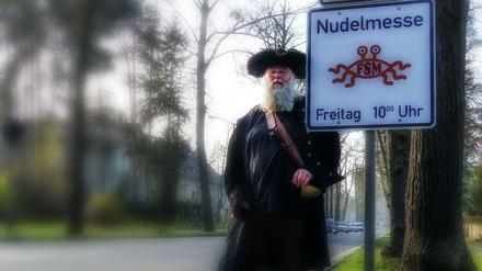 Schilda. Rüdiger Weida im Pastafari-Piratendress am noch sauberen Schild. Einige wurden beschmiert. Nun darf der Religionssatiriker eigene Masten nahe denen der Kirchen mit ihren Gottesdiensten anbringen.