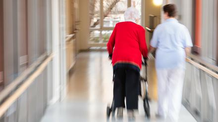 Eine Pflegerin geht mit einer Bewohnerin des Pflegeheims und einem Rollator über den Flur.