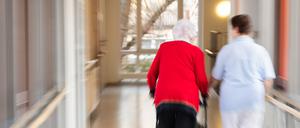 Eine Pflegerin geht mit einer Bewohnerin des Pflegeheims und einem Rollator über den Flur.