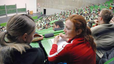 Zwei Studentinnen sitzen im Hörsaal und sprechen miteinander.