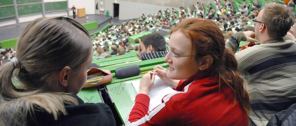 Zwei Studentinnen sitzen im Hörsaal und sprechen miteinander.