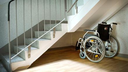 Da fehlt es noch an der Barrierefreiheit. Ein Rollstuhl steht unter einer Treppe in einem Wohnhaus. 
