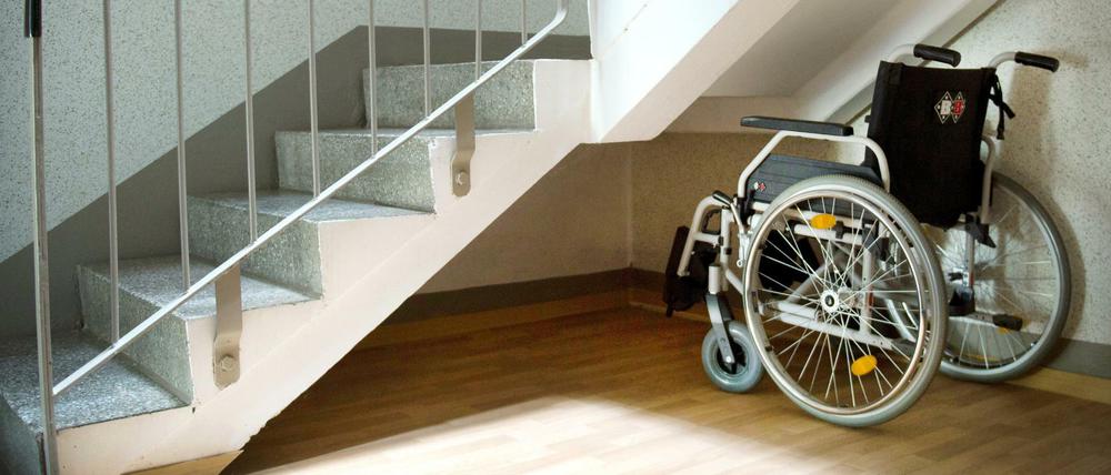 Da fehlt es noch an der Barrierefreiheit. Ein Rollstuhl steht unter einer Treppe in einem Wohnhaus. 