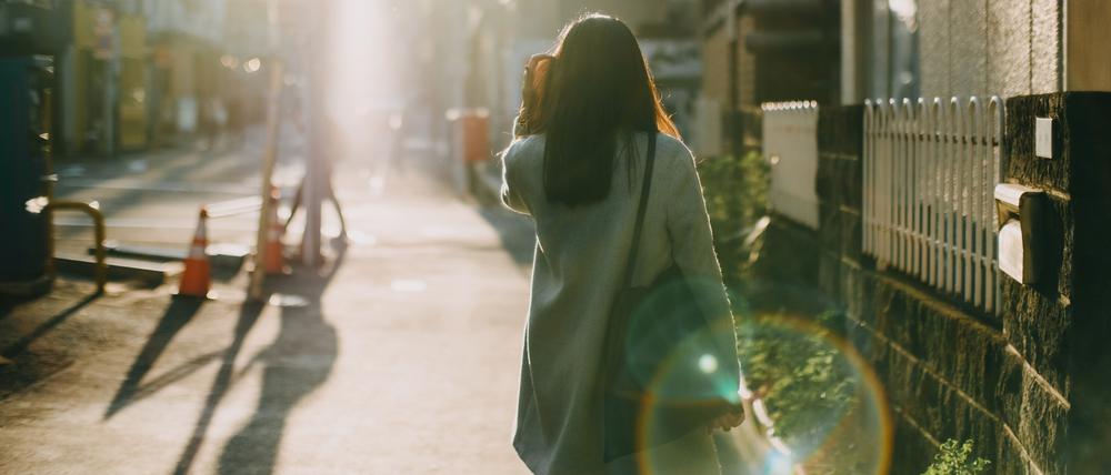 Rear view of woman leaving home to work in the early morning against warm sunlight.