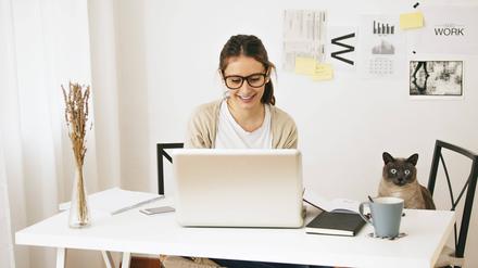 Eine junge Frau sitzt mit ihrer Katze am Schreibtisch.