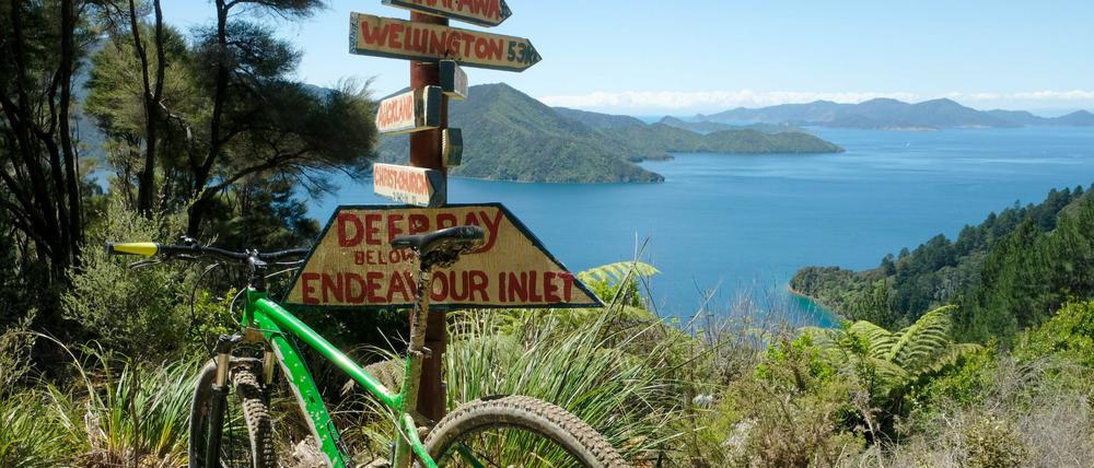 Ein Mountainbike steht an einem Wegweiser vor der Deep Bay, einer von mehreren Buchten des Endeavour Inlets.