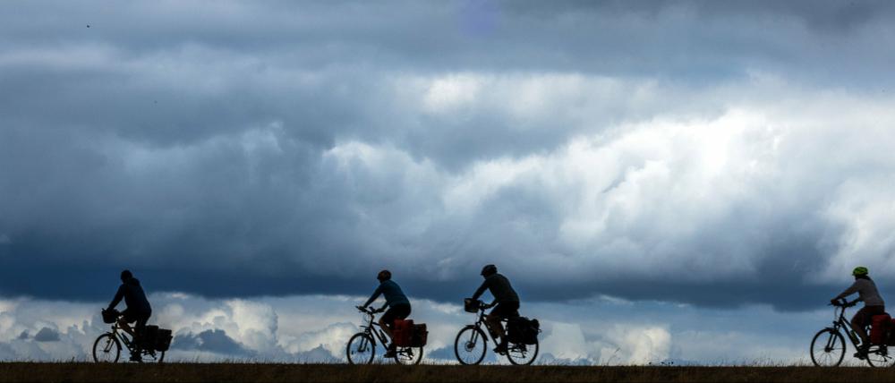 Ein Gruppe Radurlauber fährt auf dem Elbdeich vor einer dunklen Wolkenkulisse.