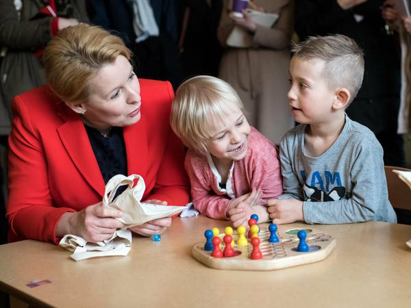 Franziska Giffey spricht mit Kita-Kindern, die vor einem Brettspiel am Tisch sitzen.