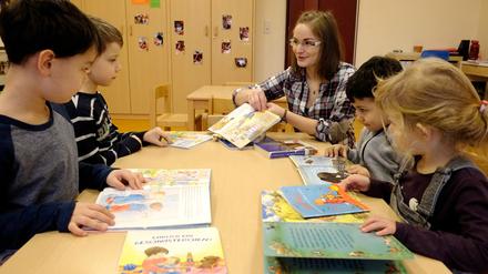 Eine Erzieherin sitzt mit vier Kindern am Tisch, die in verschiedene Bilderbücher schauen.