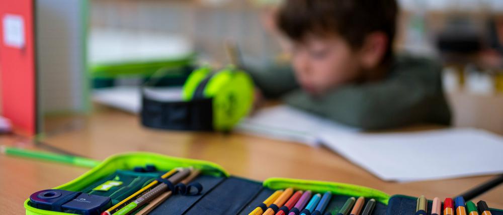 Ein Grundschüler sitzt hinter seiner aufgeklappten Federmappe am Tisch im Klassenraum.