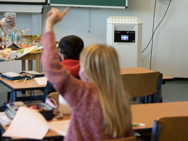 In einer Grundschule steht ein mobiler Luftfilter vor den Bänken der Schüler:innen.