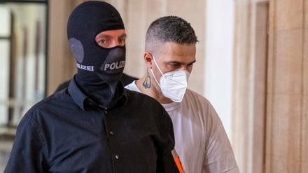 08.08.2022, Berlin: Anis Mohamed Youssef Ferchichi (r), bekannt unter dem Künstlernamen Bushido, kommt in Begleitung von Polizeibeamten zu Beginn der Verhandlung im Prozess gegen den Chef eines bekannten arabischstämmigen Clans und drei seiner Brüder in einen Gerichtssaal. Der Clanchef und seine Brüder stehen unter anderem wegen schwerer räuberischer Erpressung, Freiheitsberaubung und gefährlicher Körperverletzung vor Gericht. 