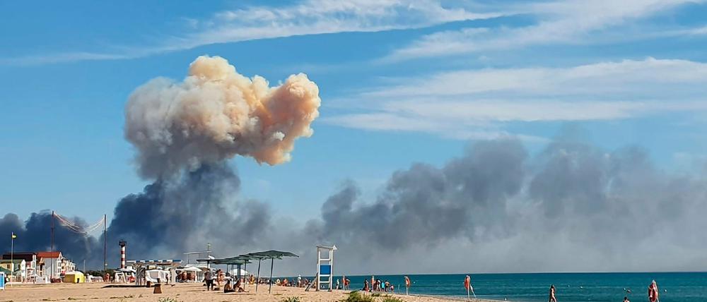 Badende mit der Rauchwolke der Explosionen im Hintergrund.