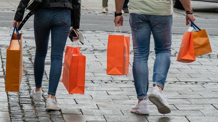 Passanten mit Einkaufstüten gehen bei Nieselwetter durch die Fußgängerzone in der Innenstadt. 